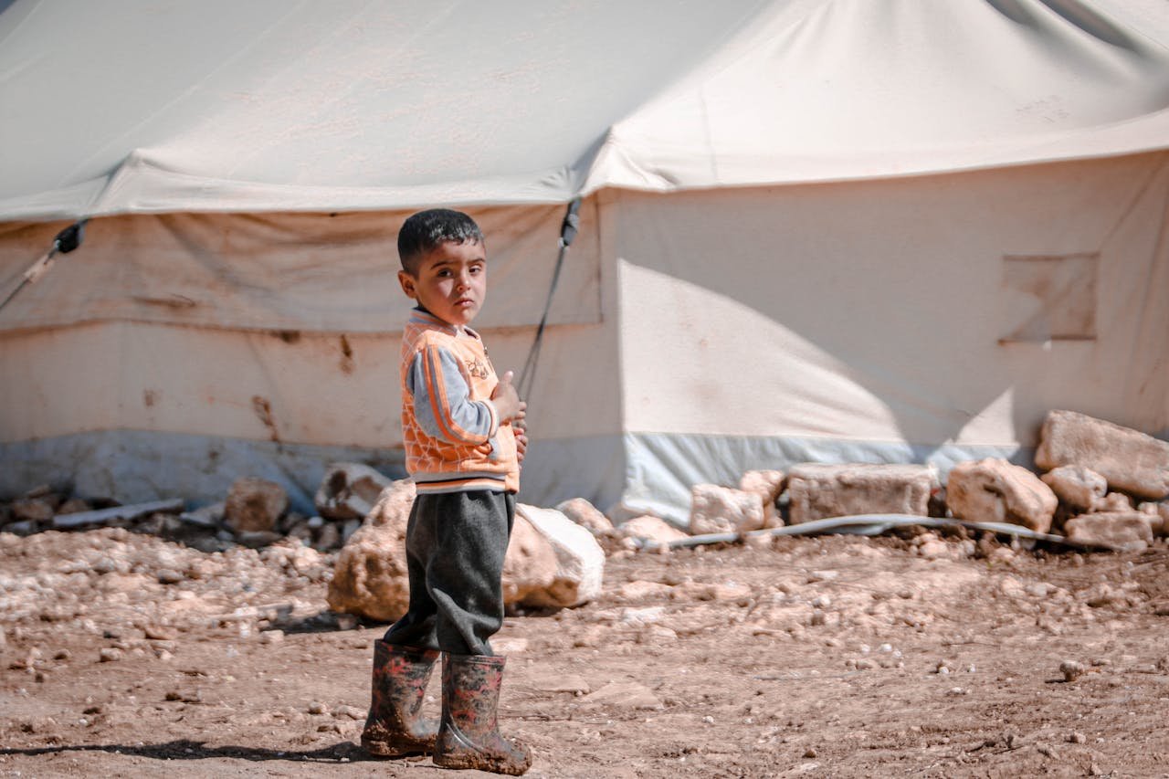A child stands near a tent in a refugee camp in Idlib, Syria, showcasing resilience and innocence.